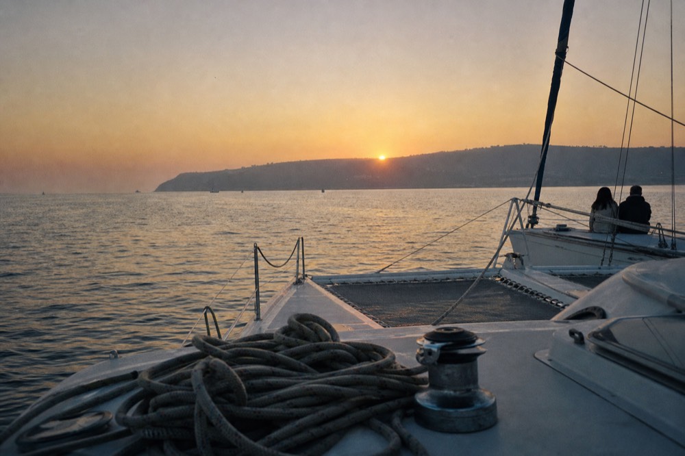 A catamaran on calm bay water as the sun sets behind Point Loma, no text, no logos, no people