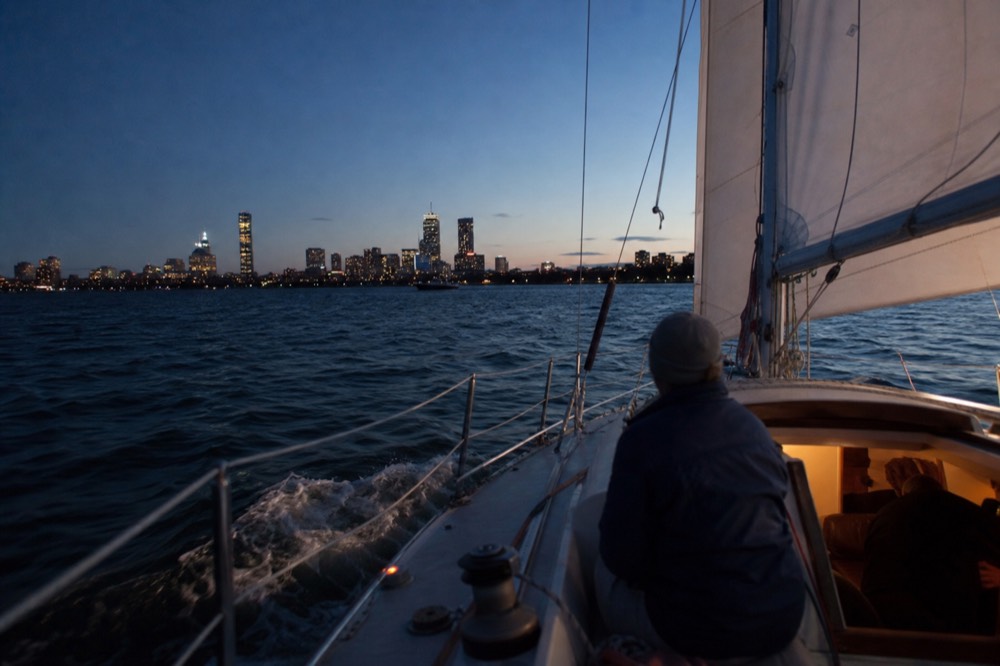 A small sailing yacht heeling gently on San Diego Bay at dusk with the downtown skyline behind, no text, no logos, no people