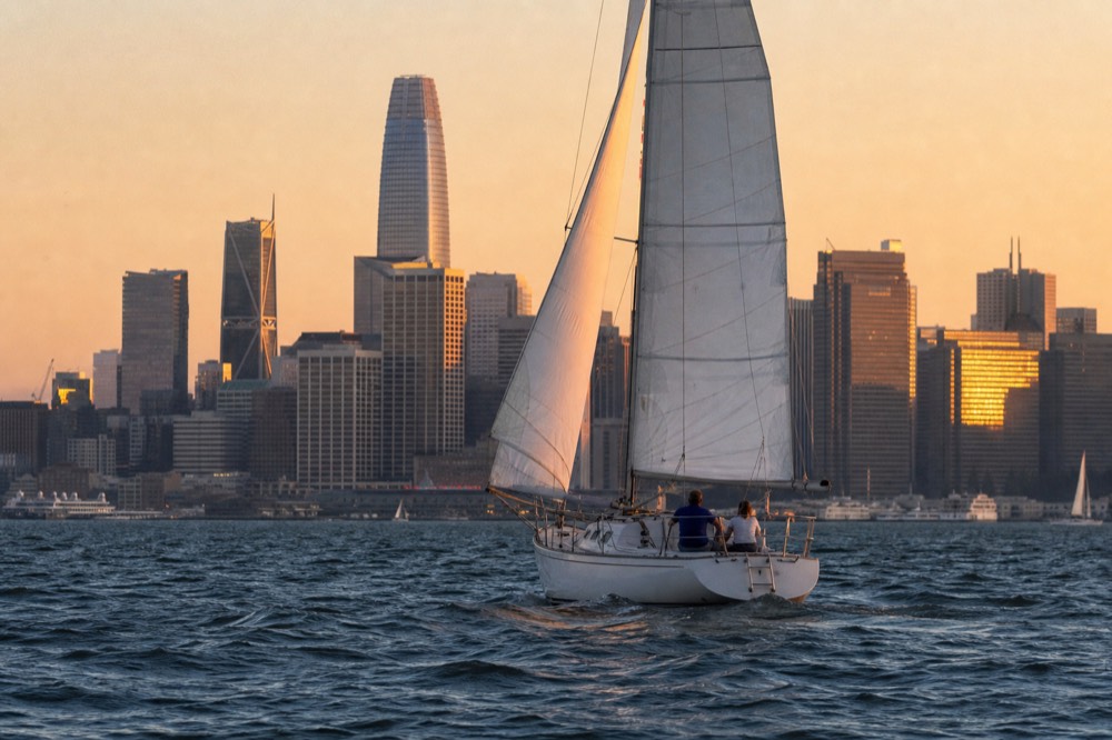 A sailing yacht passing the downtown San Diego skyline at dusk, no text, no logos, no people