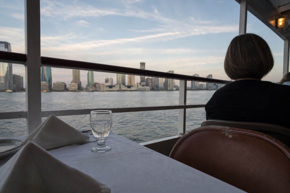 A set dinner table beside a window on a cruise boat overlooking the bay at sunset, no text, no logos, no people.