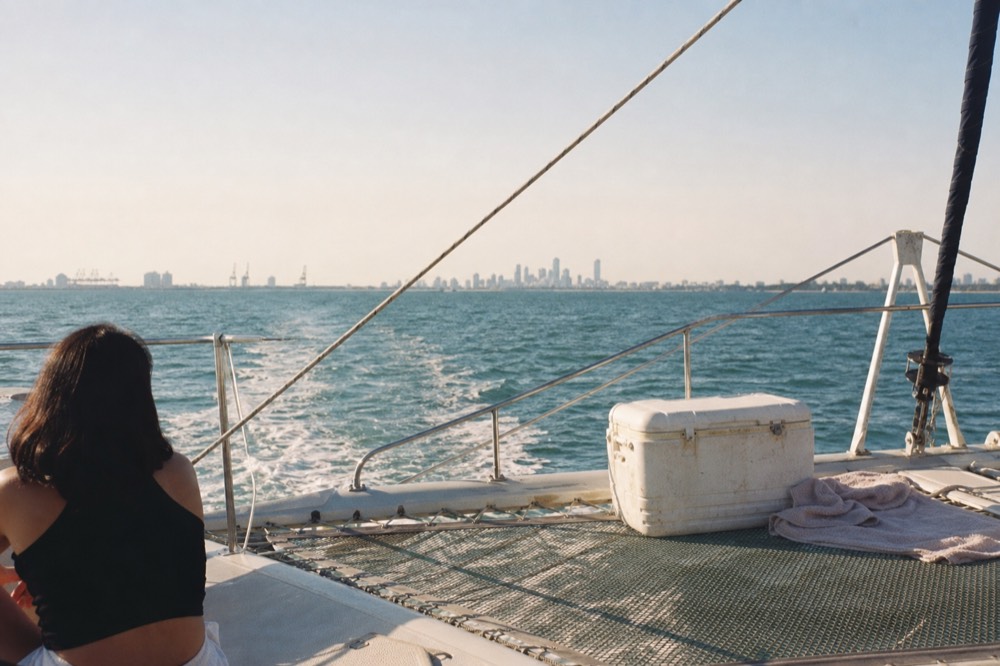Catamaran gliding across open bay water with the city skyline far in the distance, no text, no logos, no people