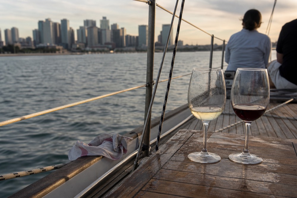 Two wine glasses on a sailboat rail with the bay and skyline in the background, no text, no logos, no people