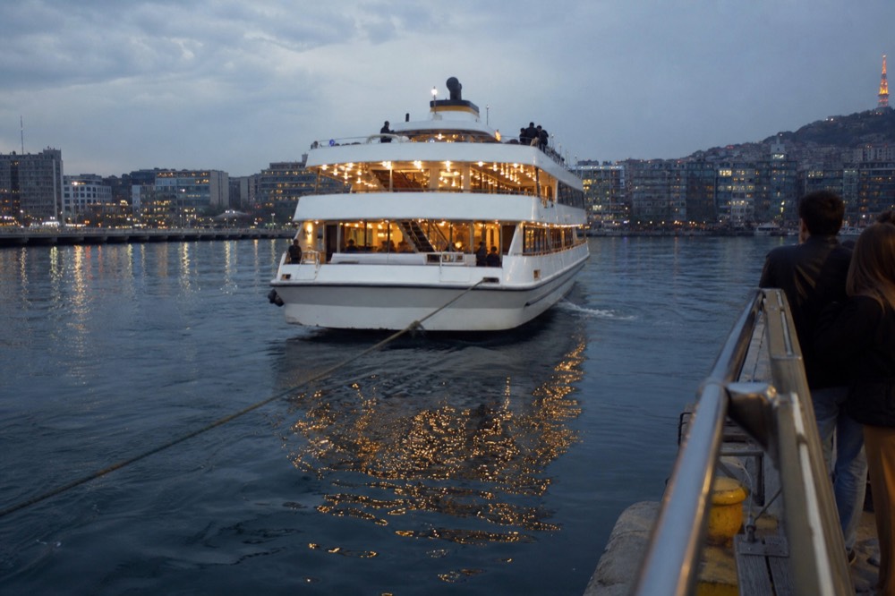 A dinner cruise boat underway on a bay at dusk with city lights reflected on the water, no text, no logos, no people