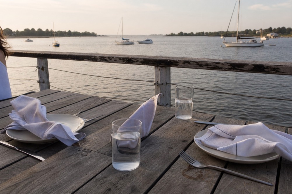 A couple's dinner table set with two place settings on an outdoor deck overlooking a bay, no text, no logos, no people