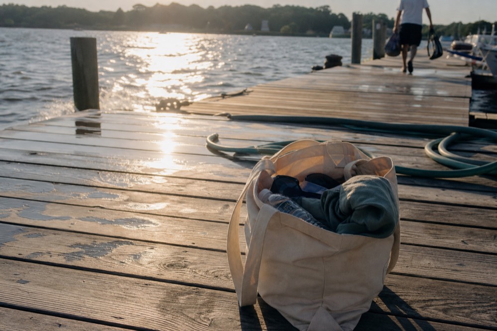 A cooler with water bottles and a packed snack bag set on a dock beside a boat, no text, no logos, no people.