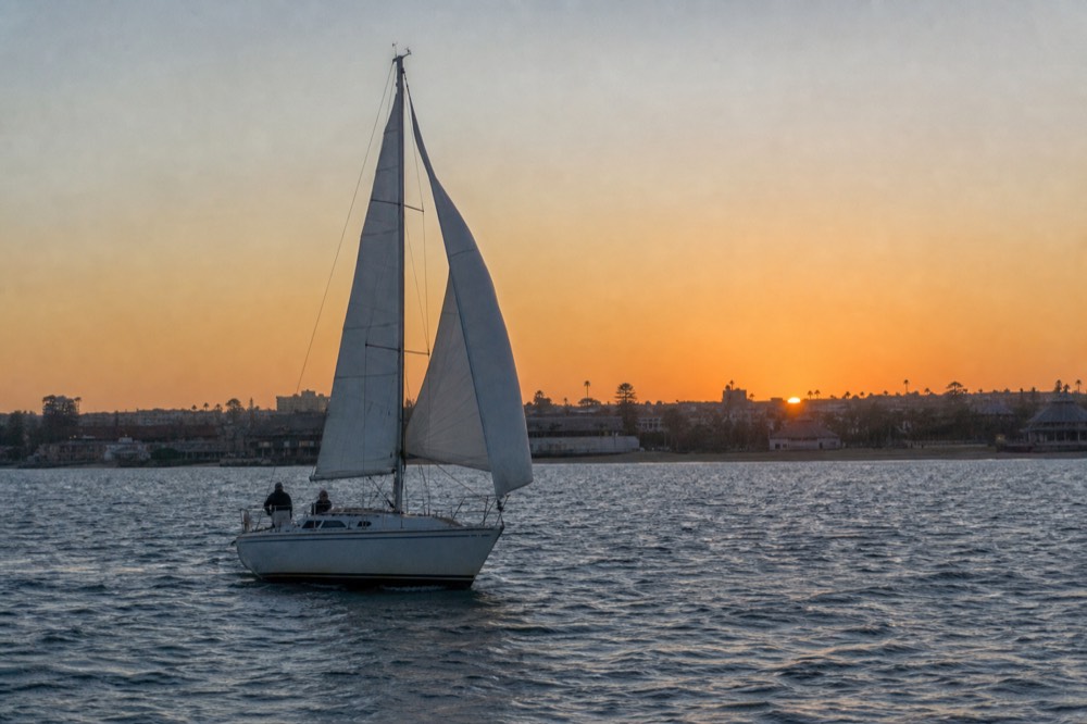 A person in a windbreaker and beanie leaning on a boat railing watching the sun set over the water, no text, no logos, no people.