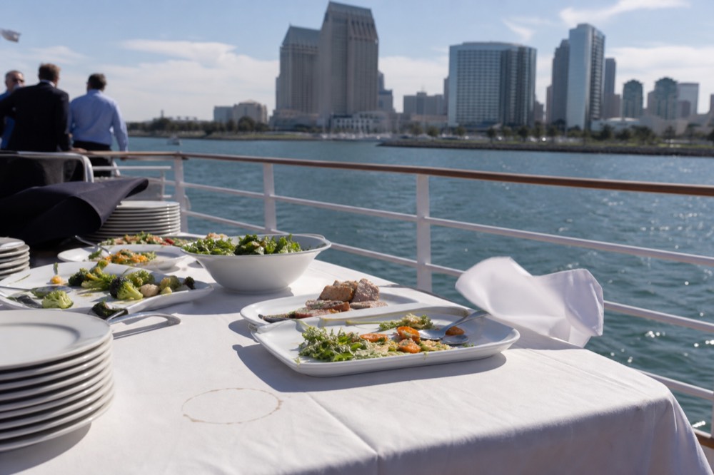 Dining table set with buffet plates beside a ship railing on San Diego Bay, no text, no logos, no people