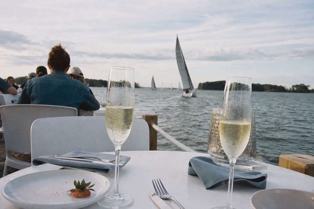 Champagne glasses on a brunch table with sailboats on the water behind, no text, no logos, no people