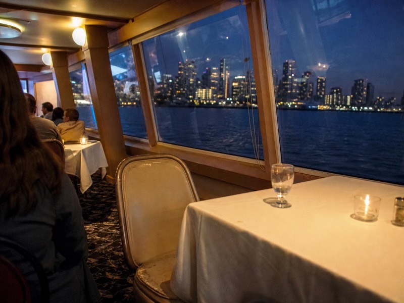 Dinner tables set by the windows of a bay cruise saloon with the San Diego skyline outside