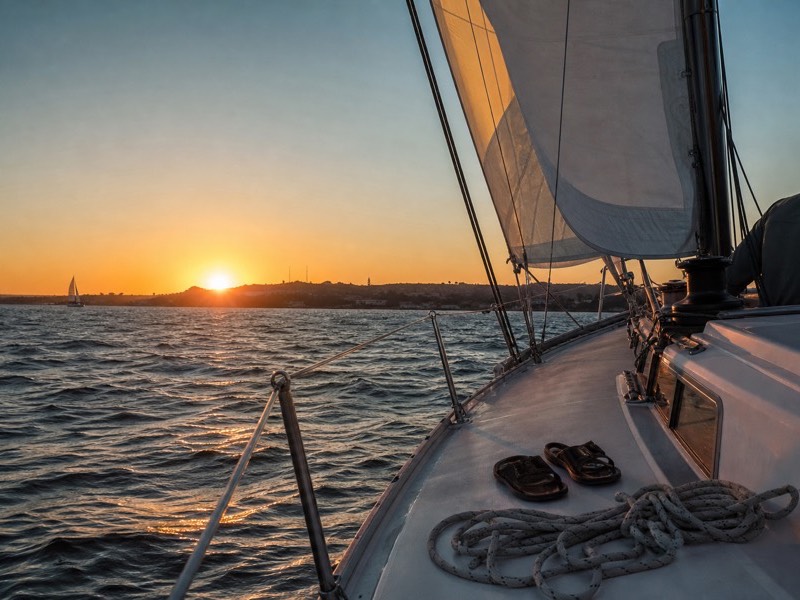 Sailboat heeling on San Diego Bay with the sun low over Point Loma