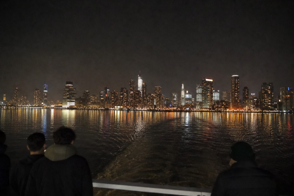 City skyline towers lit up and reflected in calm open bay water at night, no text, no logos, no people
