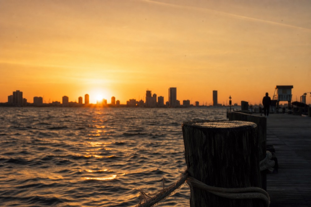 Golden sunset light over the bay with the downtown skyline silhouette behind, no text, no logos, no people