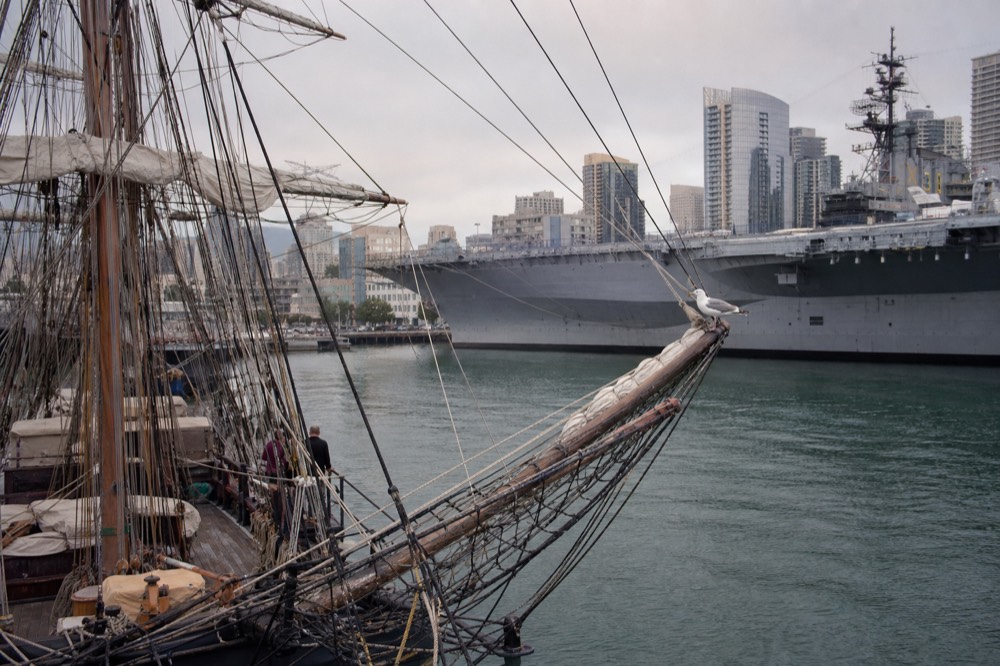 Historic tall ship and aircraft carrier docked along the downtown waterfront seen from the water, no text, no logos, no people