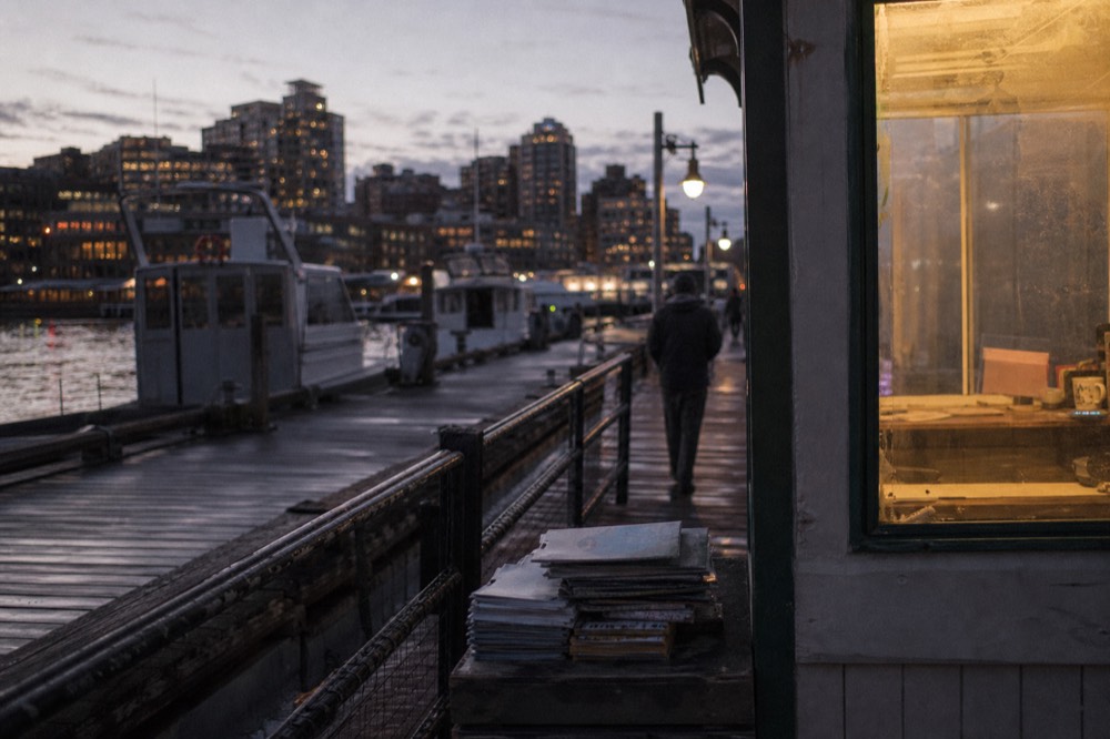 A waterfront pier with moored boats and downtown buildings beyond at dusk, no text, no logos, no people