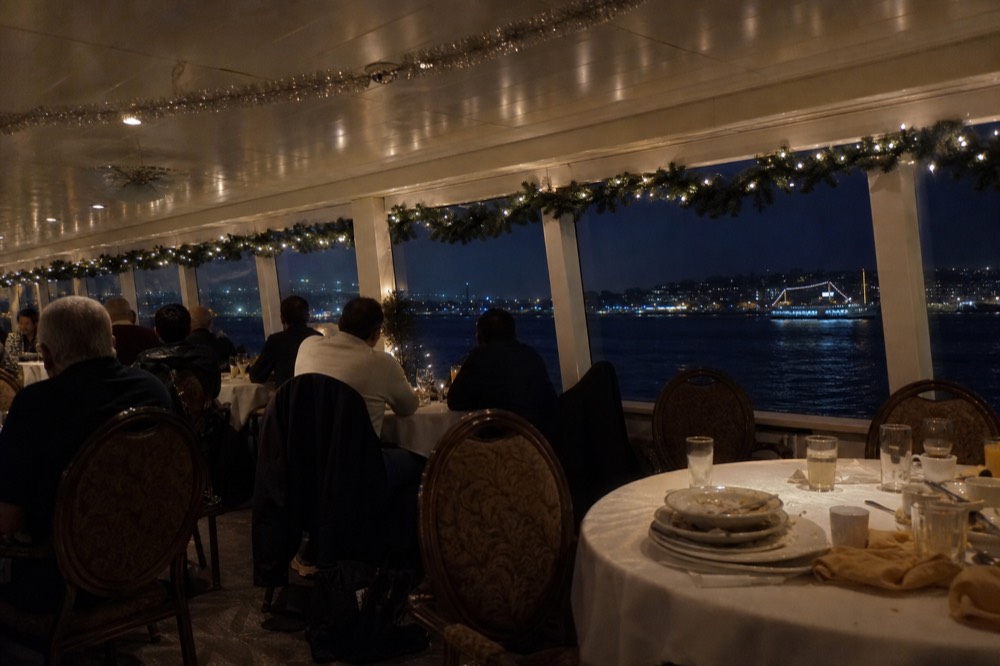 A festively decorated cruise ship dining room with holiday garlands along the windows and the bay outside, no text, no logos, no people