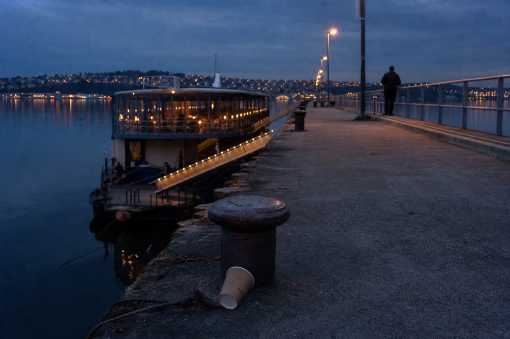 A cruise pier at dusk with a moored dining vessel and city lights reflecting on the bay water, no text, no logos, no people