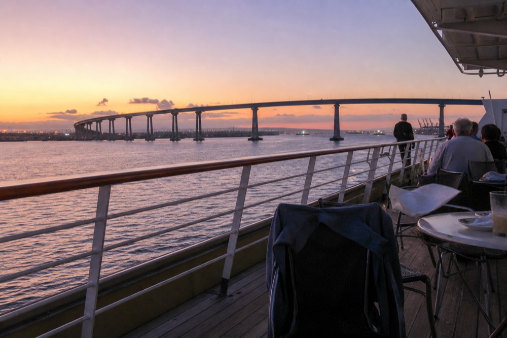 A passenger deck railing at sunset with the Coronado Bridge silhouette on the horizon, no text, no logos, no people
