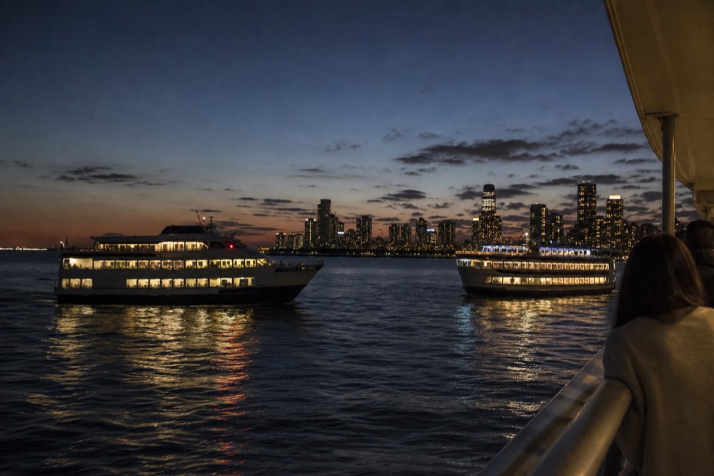 Two dinner cruise vessels passing each other on San Diego Bay with the downtown skyline at twilight, no text, no logos, no people
