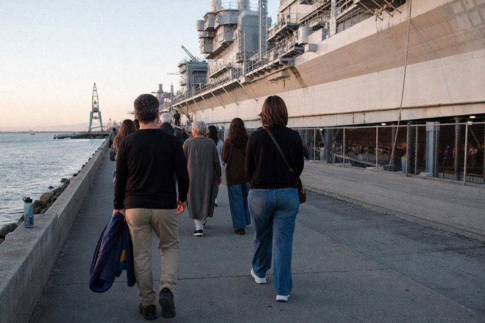 A walking tour pausing at a waterfront railing with the bay behind it, no text, no logos, no people