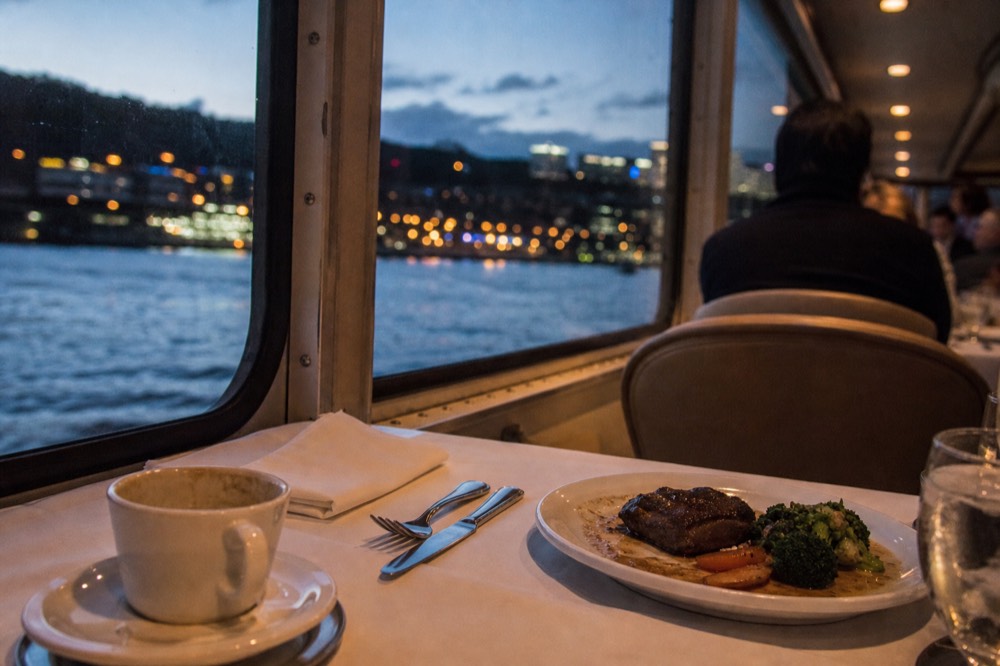 A plated dinner setting on a cruise ship table near a window with harbor views, no text, no logos, no people