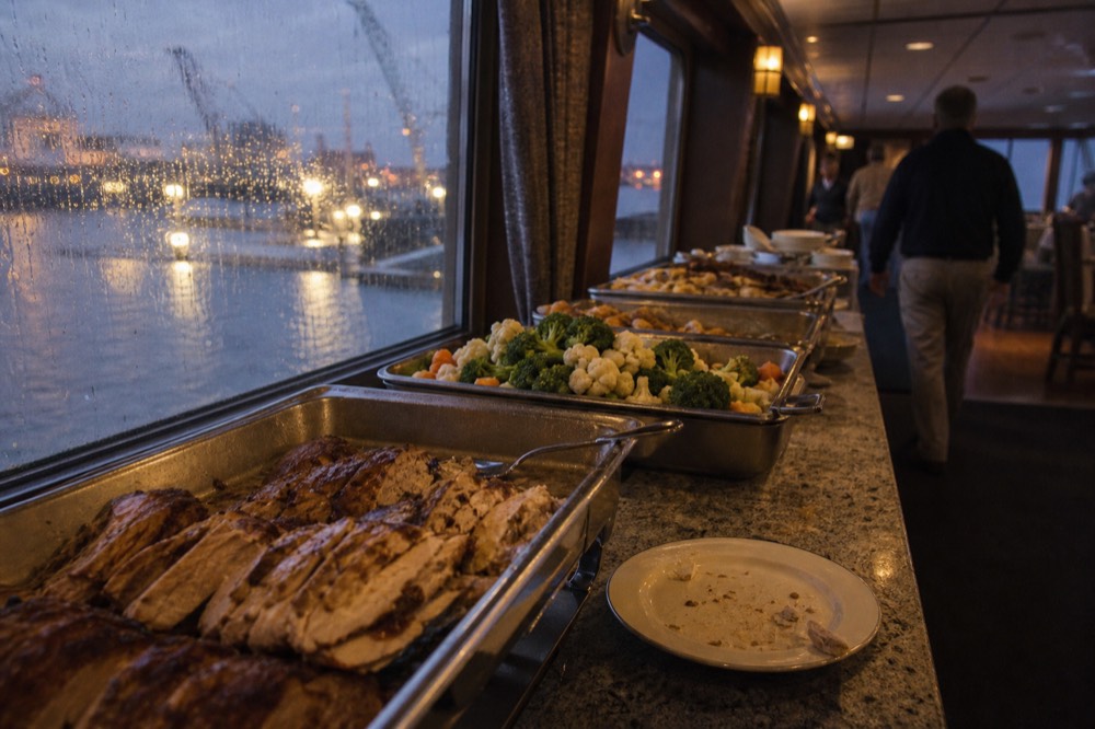 A buffet dinner spread on a cruise ship dining deck with harbor lights outside the windows, no text, no logos, no people