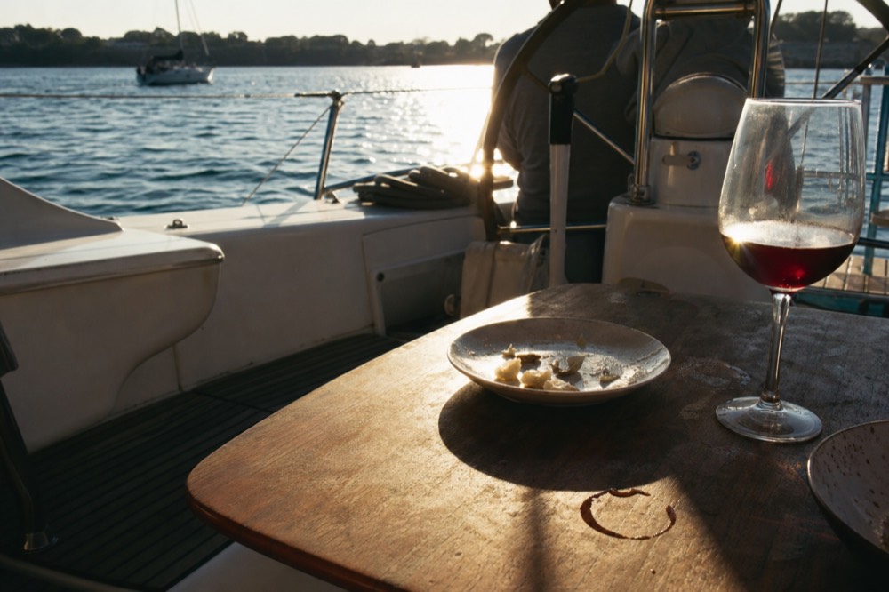 A glass of wine and a dinner plate on a cruise ship table with the bay outside the window, no text, no logos, no people