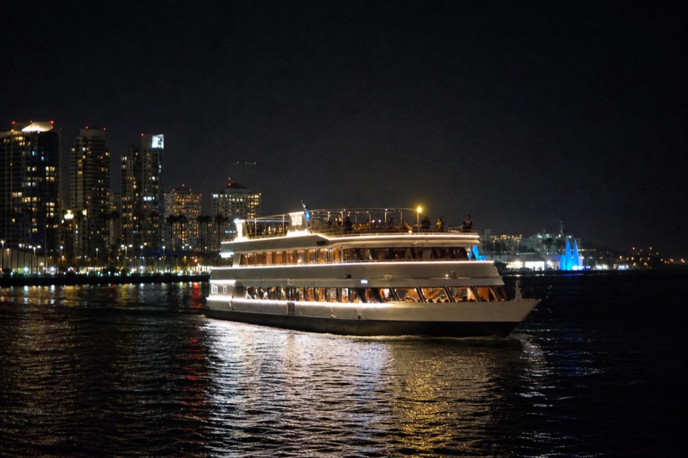 A dinner cruise boat lit at night cruising past the downtown San Diego skyline, no text, no logos, no people