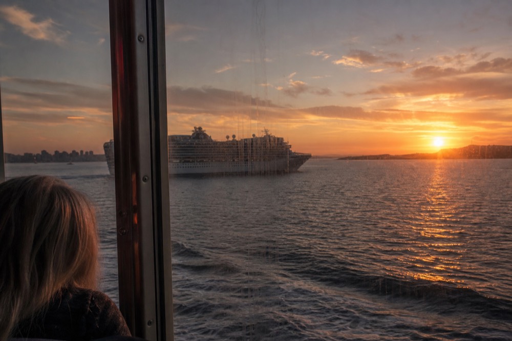 A cruise vessel crossing San Diego Bay at sunset with the city skyline behind it, no text, no logos, no people