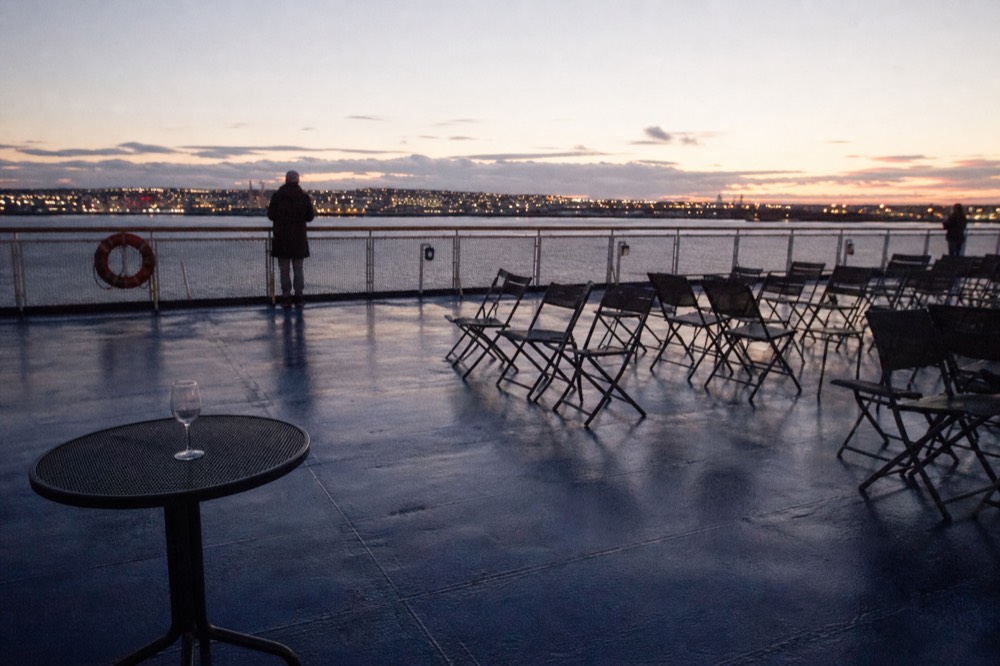 A nearly empty outdoor deck of a cruise ship on San Diego Bay at dusk with city lights beyond, no text, no logos, no people