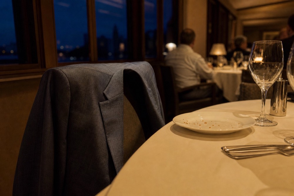A folded dress jacket draped over the back of a chair at a set dinner table on a cruise ship, no text, no logos, no people