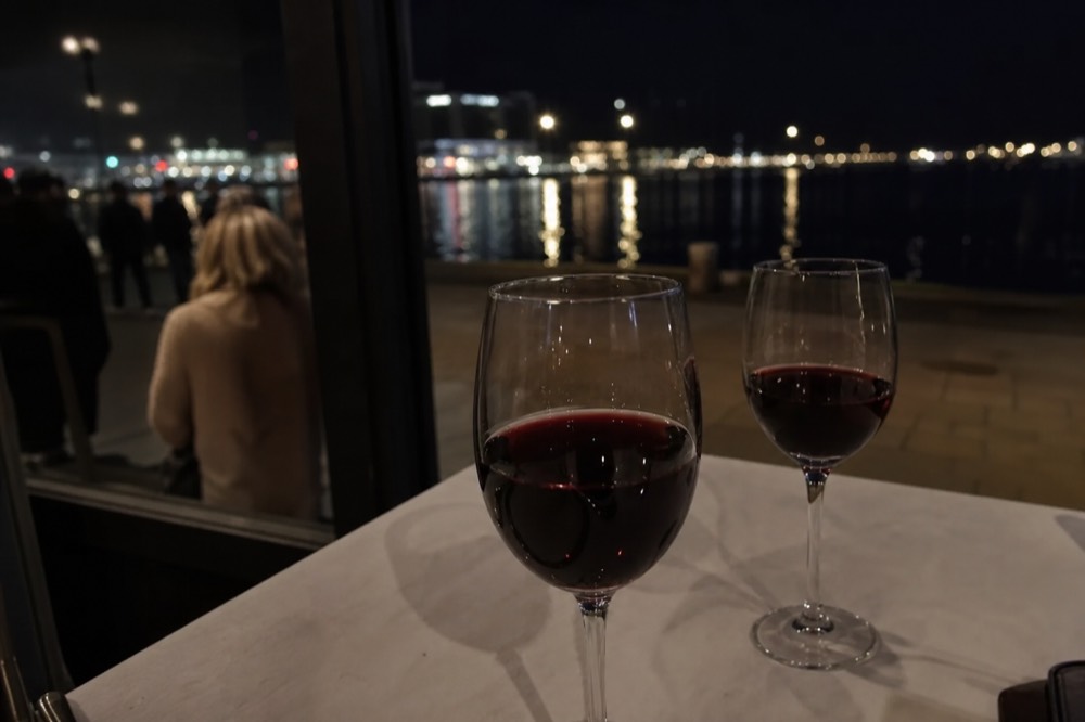 Two glasses of wine on a dinner table with the lights of the San Diego waterfront blurred through the window, no text, no logos, no people