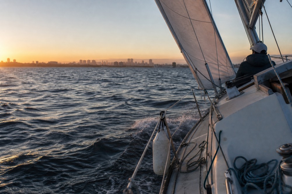 A small sailing yacht heeling gently on San Diego Bay at sunset with the city behind it, no text, no logos, no people