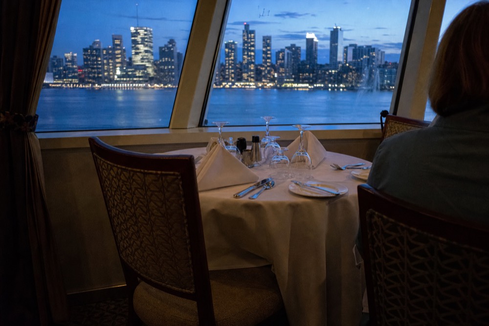 Plated dinner table setting in a cruise ship dining cabin with San Diego skyline outside, no text, no logos, no people