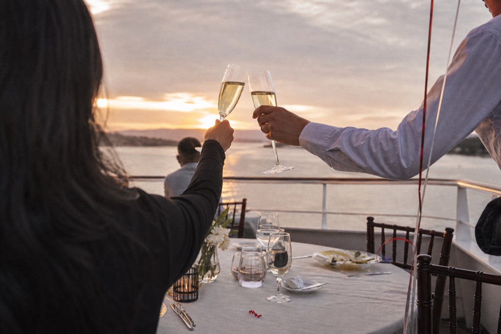 Celebration table with drinks raised on a cruise ship deck above San Diego Bay, no text, no logos, no people