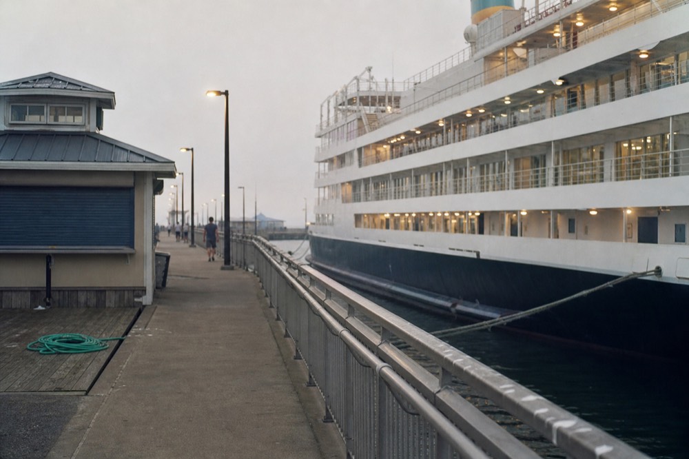 A cruise vessel departing a pier at dusk with city lights reflecting on the water, no text, no logos, no people