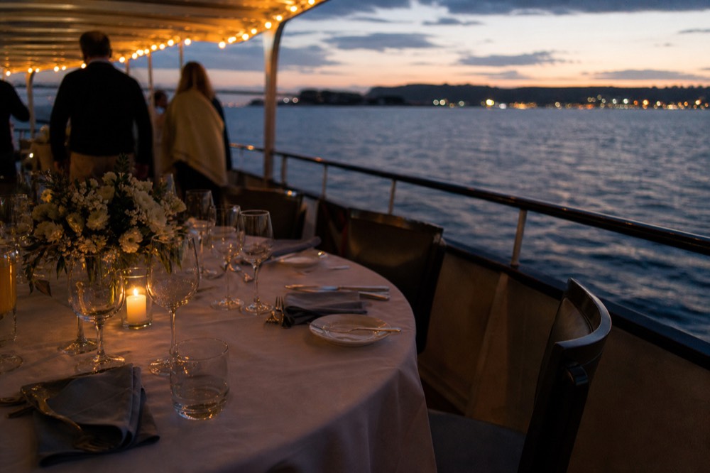 A set dinner table on the deck of a boat at dusk on San Diego Bay, no text, no logos, no people