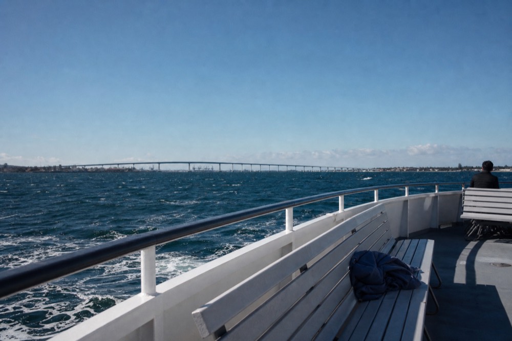 A boat on San Diego Bay under a clear sky with the Coronado Bridge in the distance, no text, no logos, no people