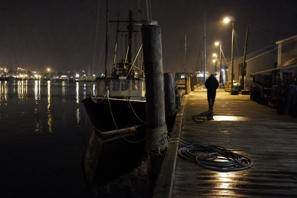 Lit pier structure extending into San Diego Bay at night with reflections on calm water, no text, no logos, no people