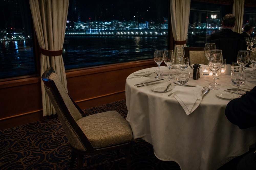 Set dinner table on a cruise ship with city lights visible through windows at night, no text, no logos, no people