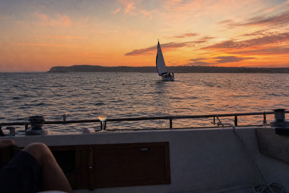 Sailboat silhouette on San Diego Bay at dusk with warm sky over the water, no text, no logos, no people