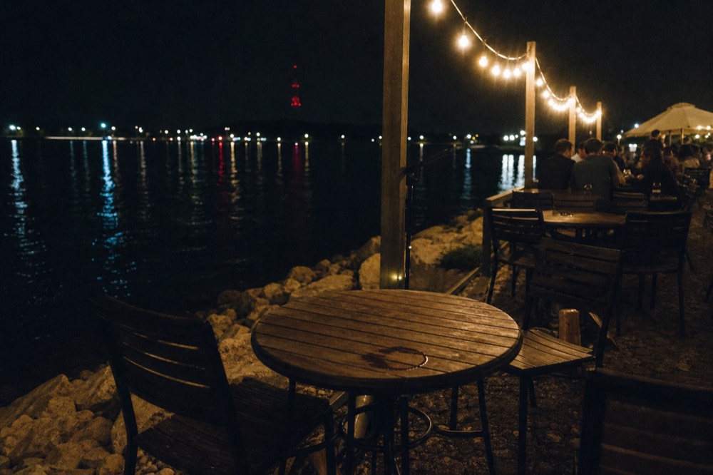 Waterfront restaurant terrace at night with string lights overlooking San Diego Bay, no text, no logos, no people