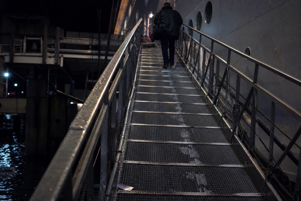 A steep metal boarding gangway leading from a pier to a cruise ship deck at night, no text, no logos, no people