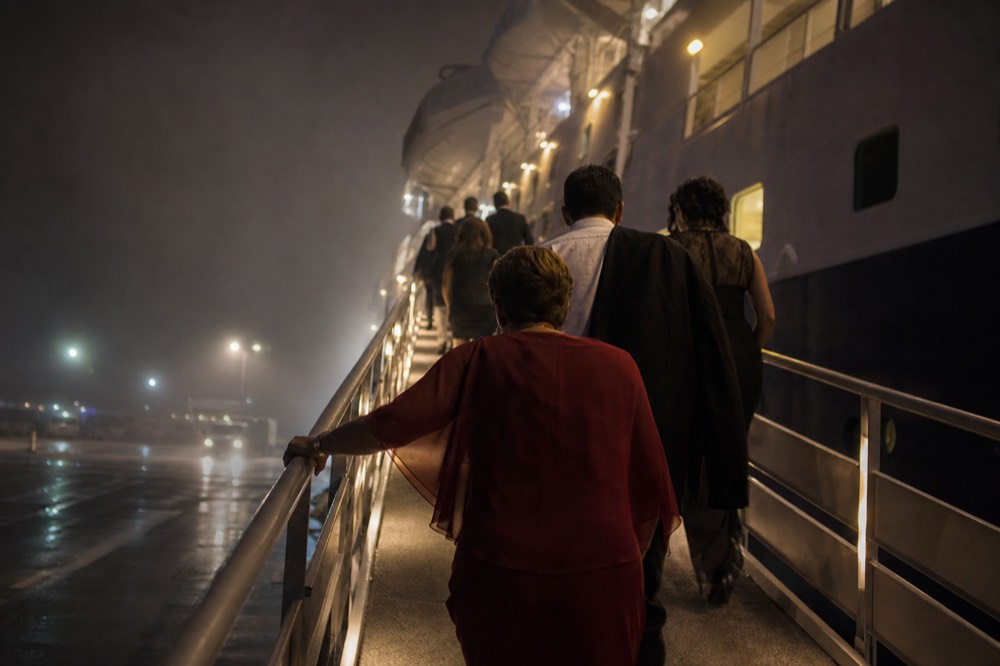 Passengers in evening wear climbing a lit boarding ramp toward a cruise ship at night, no text, no logos, no people